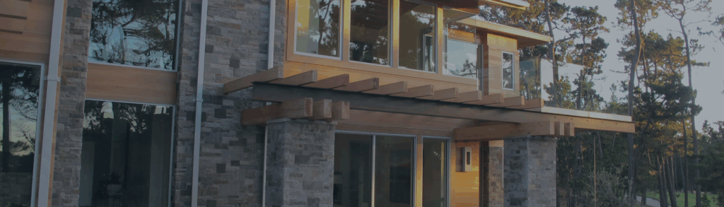 Modern two-story home with Shakertown® natural cedar siding, stone columns, large windows, and wooden pergola accents surrounded by trees banner footer